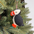 Handmade puffin felt ornament in black, white, and orange hanging on a green Christmas tree branch.
