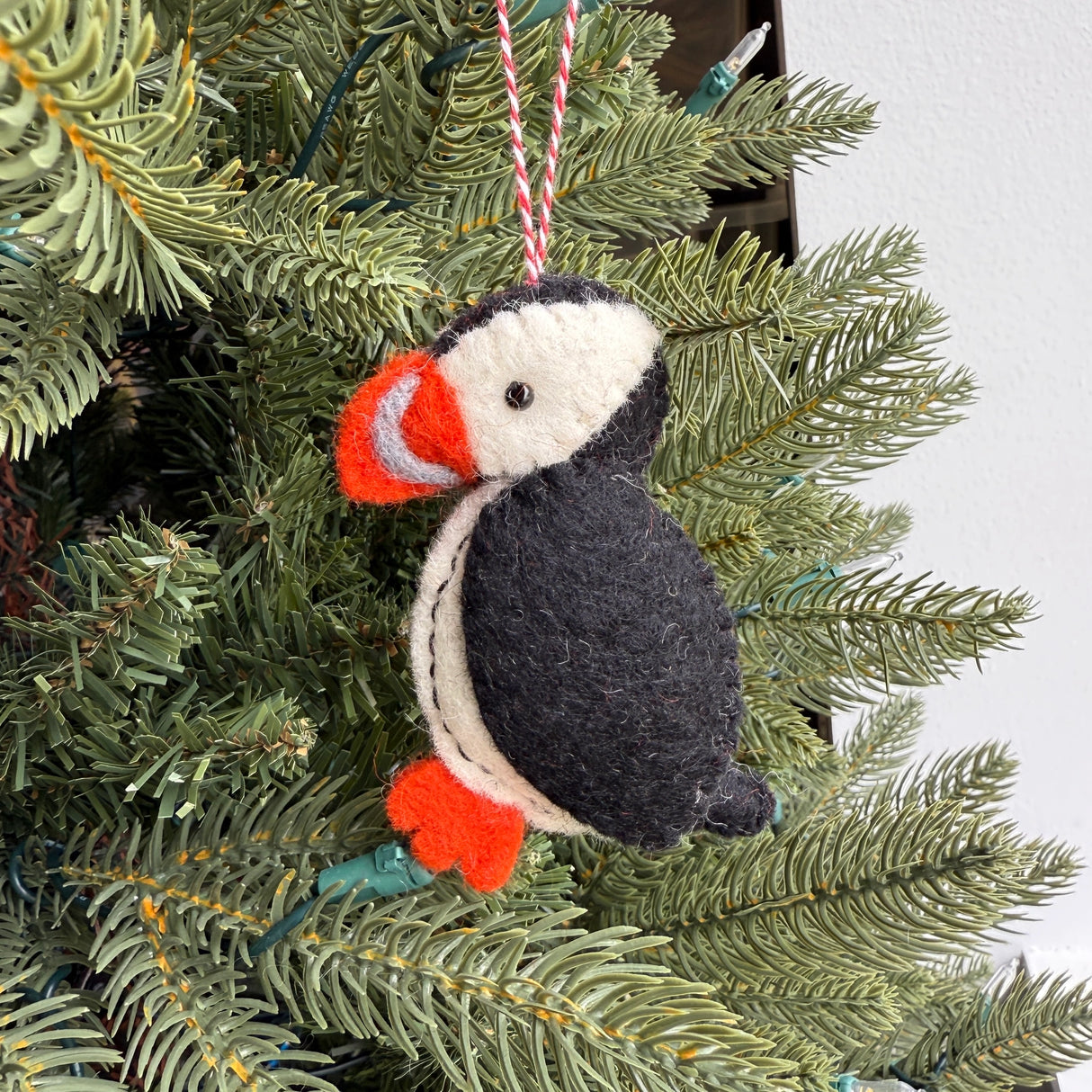 Handmade puffin felt ornament in black, white, and orange hanging on a green Christmas tree branch.