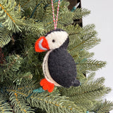 Handmade puffin felt ornament in black, white, and orange hanging on a green Christmas tree branch.