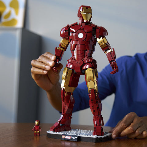 Adult hands posing a detailed Iron Man Mark 3 LEGO figure standing on a display base on a wooden table