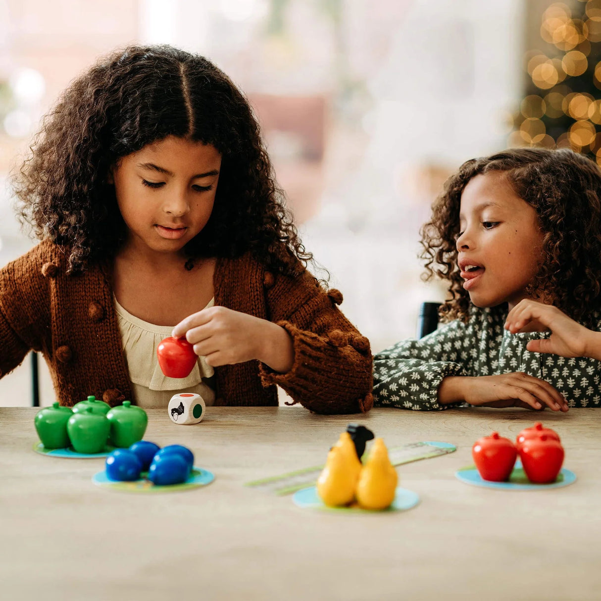 Two children playing with colorful wooden fruit pieces and a raven figure on a table in a cooperative game setting