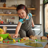 Young girl playing Orchard Game with colorful fruit pieces and wooden baskets on a table in a cozy kitchen setting