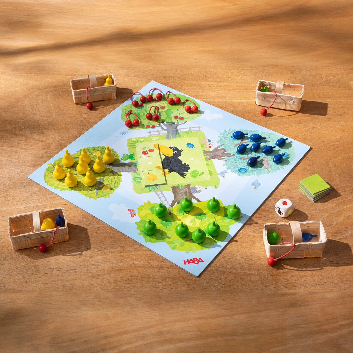 Colorful fruit pieces and baskets set on a game board featuring a raven, ready for cooperative play in Orchard Game.