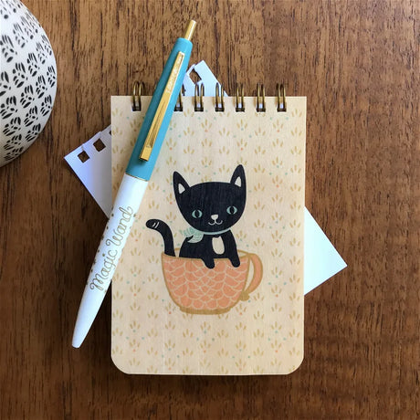 Mini Wood Notebook | Cuppa Kitty with black cat in a cup design on eco-friendly birch cover on wood table.