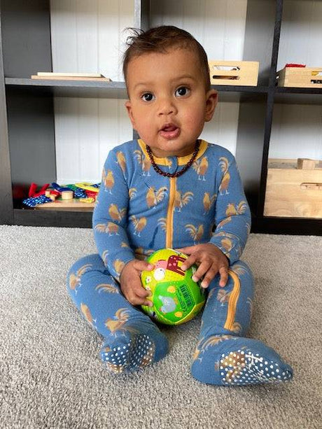 Baby Ball | On the Farm held by baby sitting on carpet in blue rooster pajamas, encouraging motor skills development.