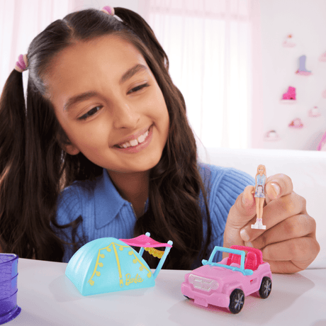 Girl playing with Mini BarbieLand Camping set featuring a pink vehicle, blue tent, and Barbie doll for imaginative play.
