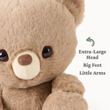 Close-up of a soft, small plush bear with an extra-large head, big feet, and little arms in light brown color