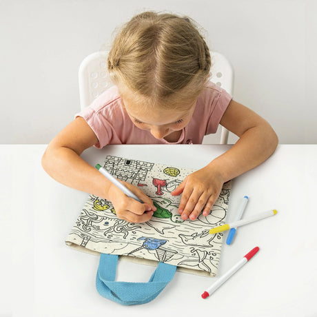 Young girl coloring a canvas tote bag with markers, showcasing the Kit & Cadoodle Color-In Tote Bag creative activity.