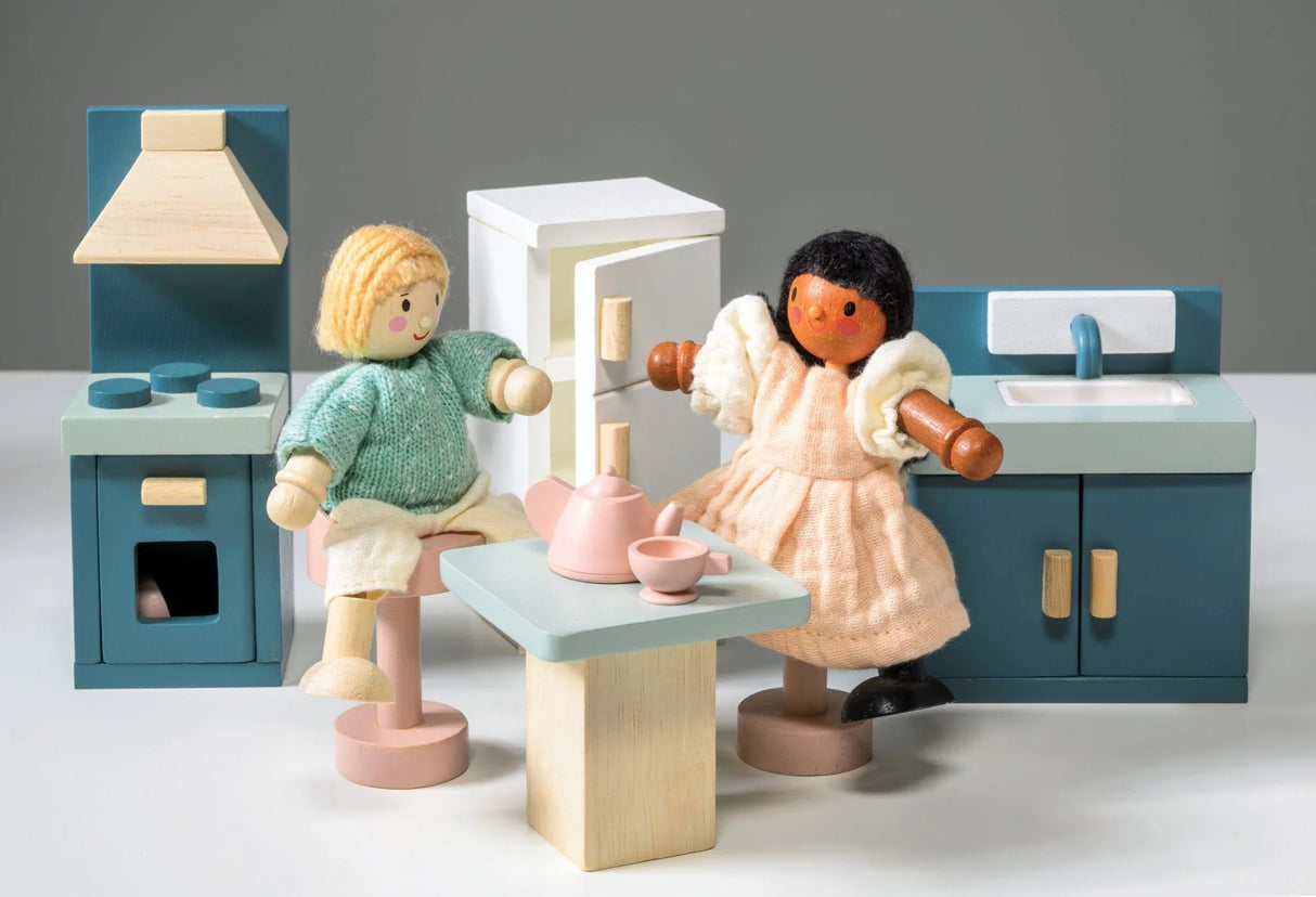 Wooden doll house kitchen set with two dolls, stove, fridge, sink, table, and tea set in soft pastel colors