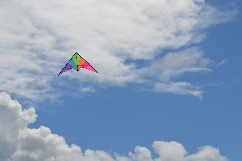 Colorful kite soaring high in a partly cloudy blue sky on a bright day