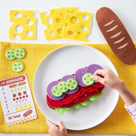 Child assembling felt sandwich with cucumber and cheese pieces using Math Sandwich educational game pieces on white plate.
