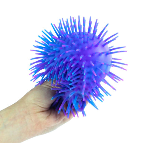 Hand squeezing a purple and blue spikey Tutti Fruiti Puffer Ball showing its unique sensory texture and form.