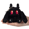 Small black plush creature with large red starry eyes, two antennae, long ears, and gray paw details held in hand