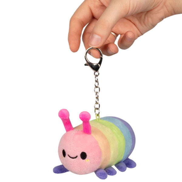 Small plush rainbow caterpillar keychain with pink face, purple legs, and smiling expression held by hand