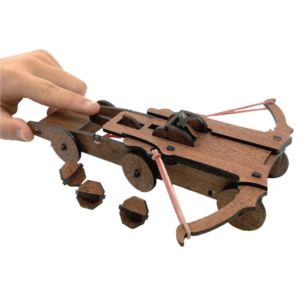Hand assembling a wooden mini crossbow model inspired by Leonardo Da Vinci with small wheels and rubber bands