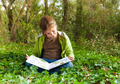 Child reading an illustrated book while sitting among greenery in a forest