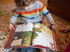 Child in a striped sweater reading an open illustrated book on a colorful rug