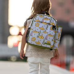 Child walking outdoors wearing a backpack with yellow submarine and seaweed pattern on a light background