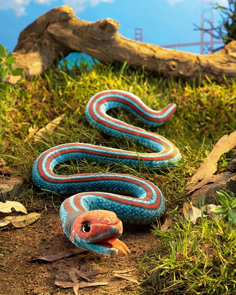 San Francisco Garter Snake Puppet with coral and turquoise colors, movable mouth, and weighted body on grass and leaves.