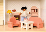 Miniature dollhouse sitting room featuring sofa, armchair, coffee table, lamp, fireplace, bookcase, and a doll figure