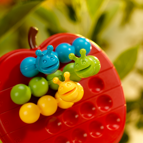 Apple Twist game board with colorful smiling caterpillar pieces arranged on red apple-shaped puzzle.