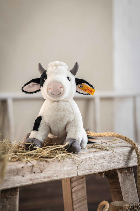 Cow Cobb plush toy sitting on a wooden table with a friendly smile and soft grey hooves.