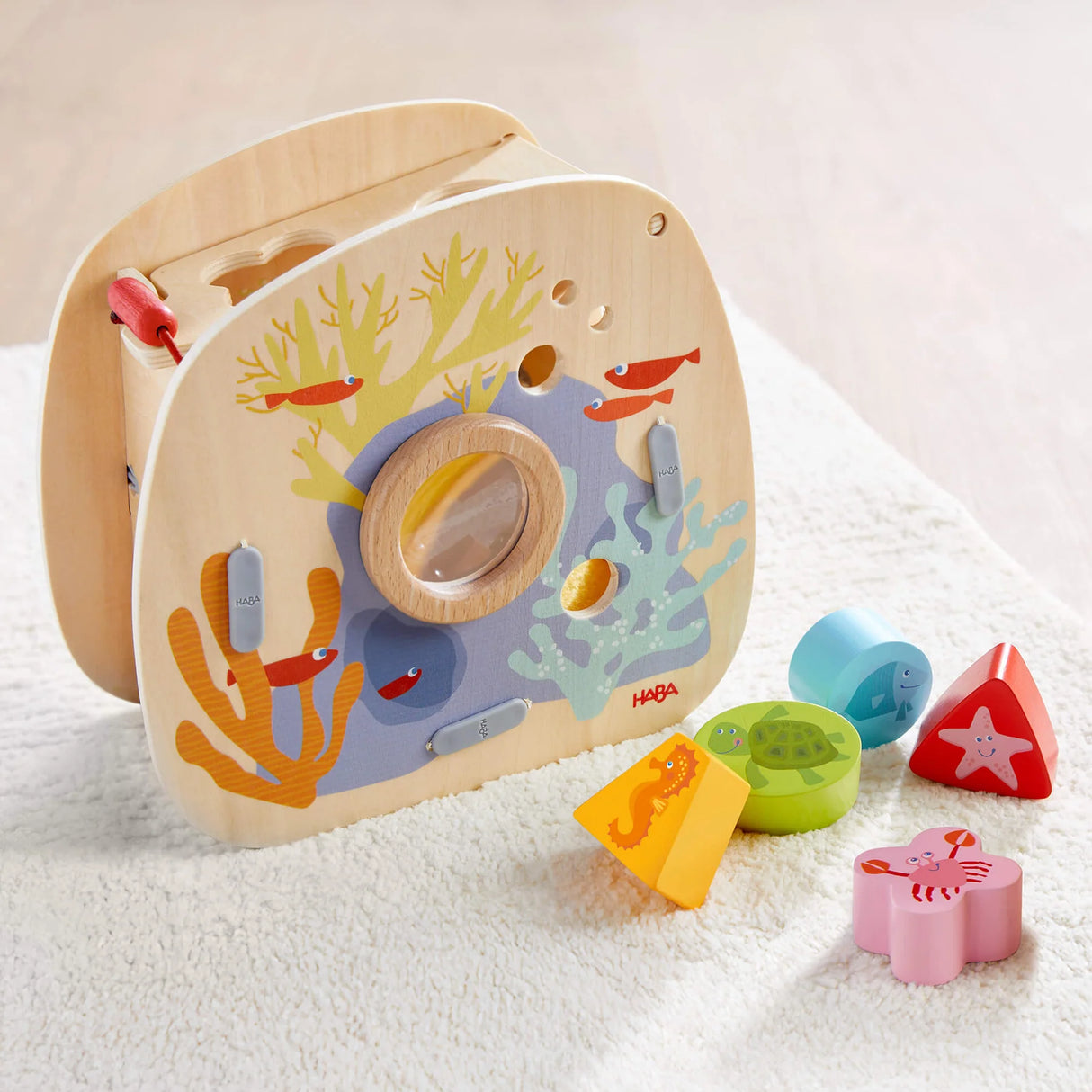 Wooden underwater shape sorter with sea creature blocks including turtle, starfish, crab, and seahorse on a soft surface