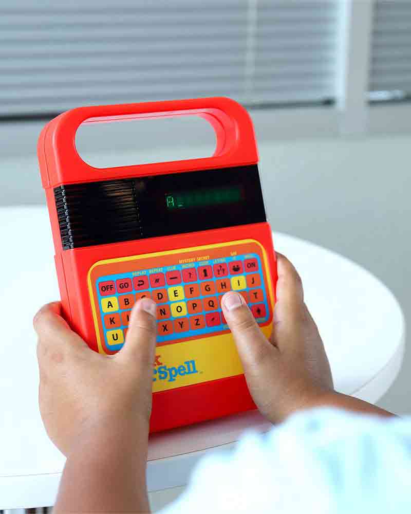 Child playing with classic Speak & Spell toy featuring retro 80s design and speech synthesizer technology.