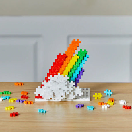 Plus Plus Rainbow 240pc building blocks creating a colorful 3D rainbow on a wooden surface with scattered pieces.