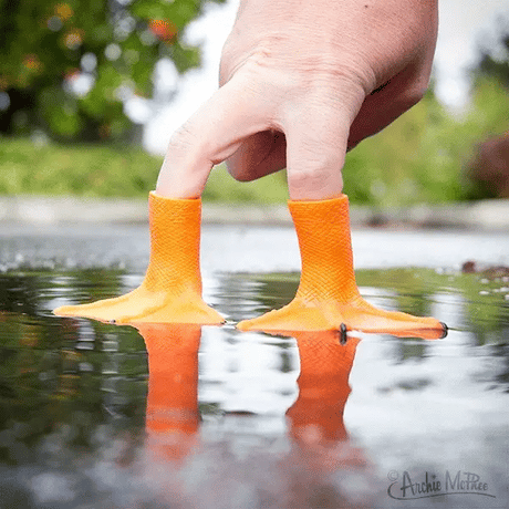 Hand wearing two bright orange Duck Foot finger puppets walking through a puddle outdoors.