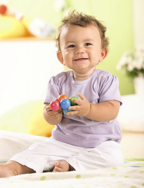 Baby smiling and holding colorful Magica Wooden Clutching Toy made of safe, hand-crafted wooden balls for teething.