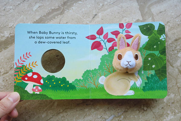 Baby Bunny with Finger Puppet board book open to colorful nature scene with plush bunny and peek-a-boo hole.