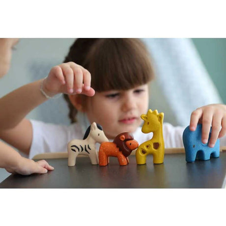 Child playing with colorful wooden Wild Animals set including lion, elephant, zebra, and giraffe on a table.
