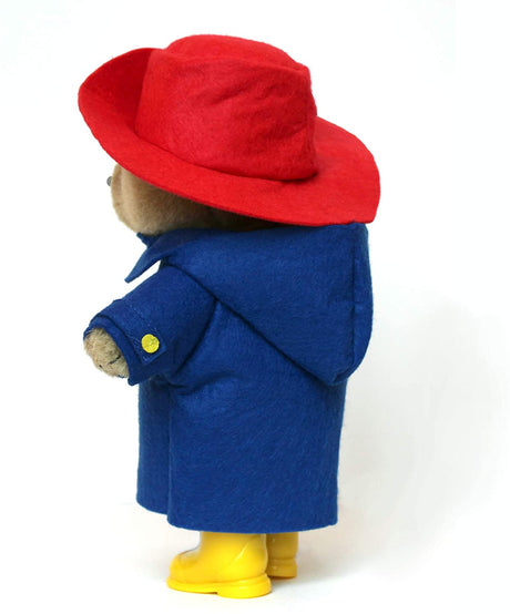 Paddington Bear plush wearing a red felt hat, blue coat with wooden toggles, and yellow Wellington boots side view.