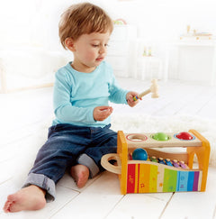 Toddler playing with the Pound & Tap Xylophone, a colorful wooden musical toy with balls and mallet for sound exploration.