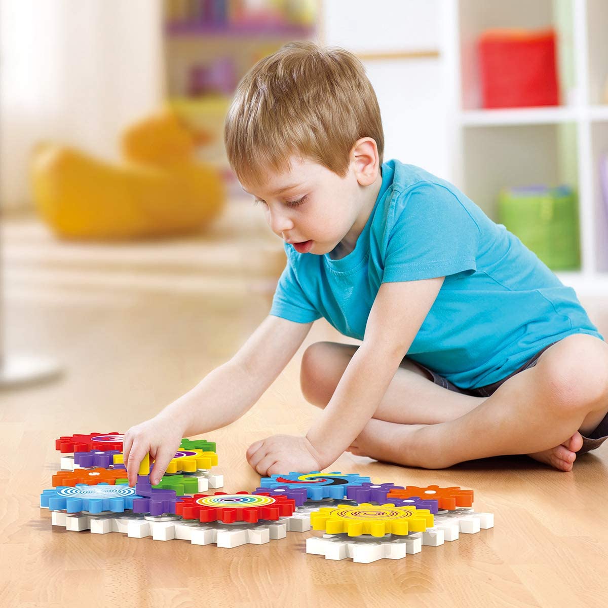 Young child playing with colorful interlocking pieces and spinning gears of Kaleido Gears on the floor.