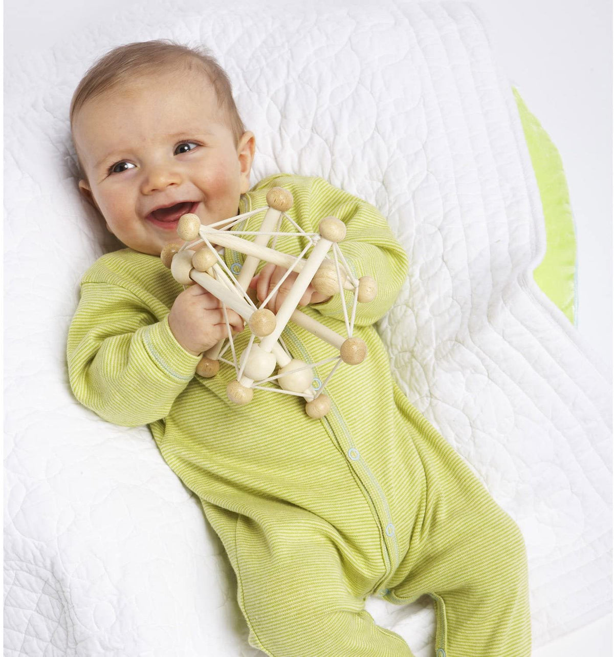 Baby in green onesie holding and playing with Natural Skwish wooden toy with beads and strings.