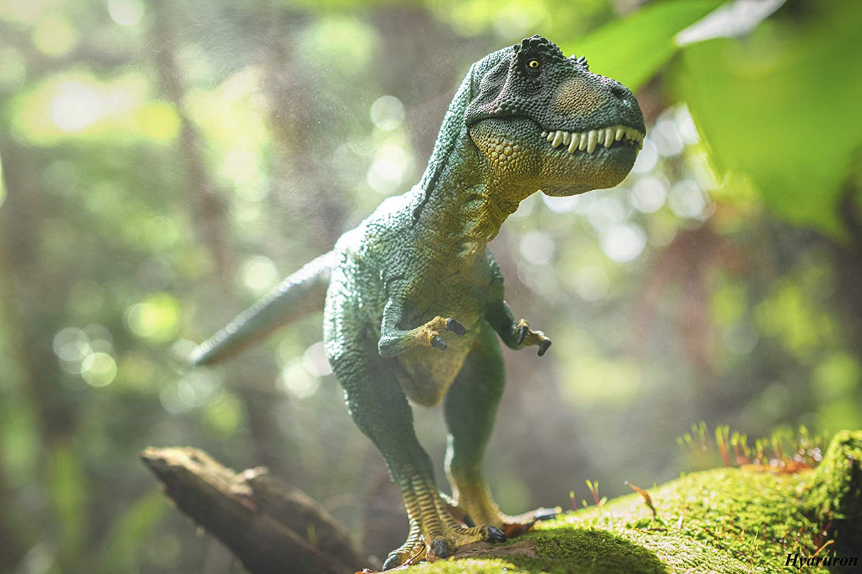 T Rex Green toy dinosaur standing on mossy log in natural forest setting, detailed and lifelike figure.
