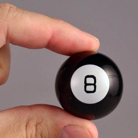 Hand holding the World's Smallest Magic 8 Ball, a tiny black fortune-telling toy for making decisions.