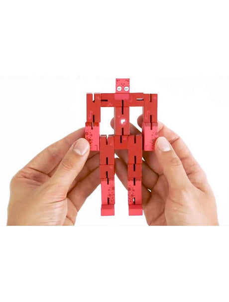 Hands holding a red wooden alien puzzle figure from the Puzzle Planet Alien brainteaser toy.