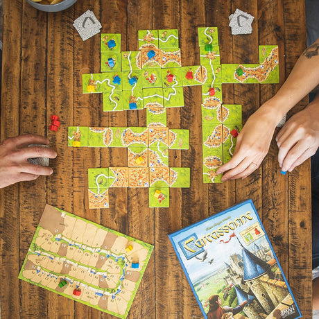 Carcassonne board game setup with tiles, followers, and score track on a wooden table during gameplay.