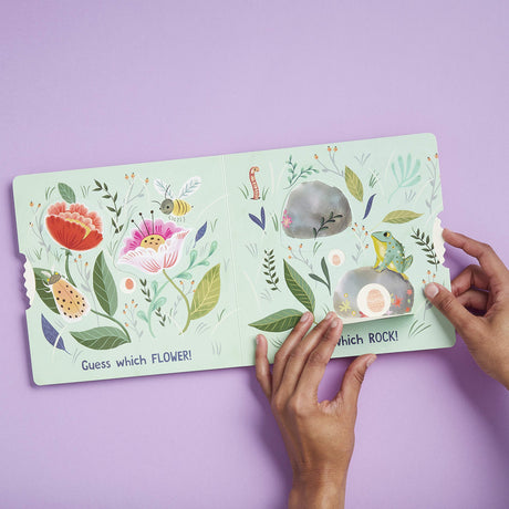 Hands holding the interactive toddler board book Eggs are Everywhere with colorful flowers and rocks illustrations.