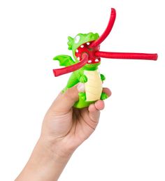 Hand holding a green Curly Pop Dragon toy with red flames popping out, designed for kids ages 5 and up.