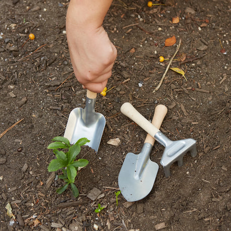 Hand using shovel in soil with rake and spade nearby in Gardening Tool Set for small gardens.