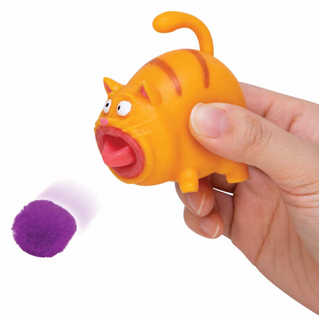 Hand squeezing the orange Hairball Kitty toy shooting a purple pom pom hairball for playful fun.