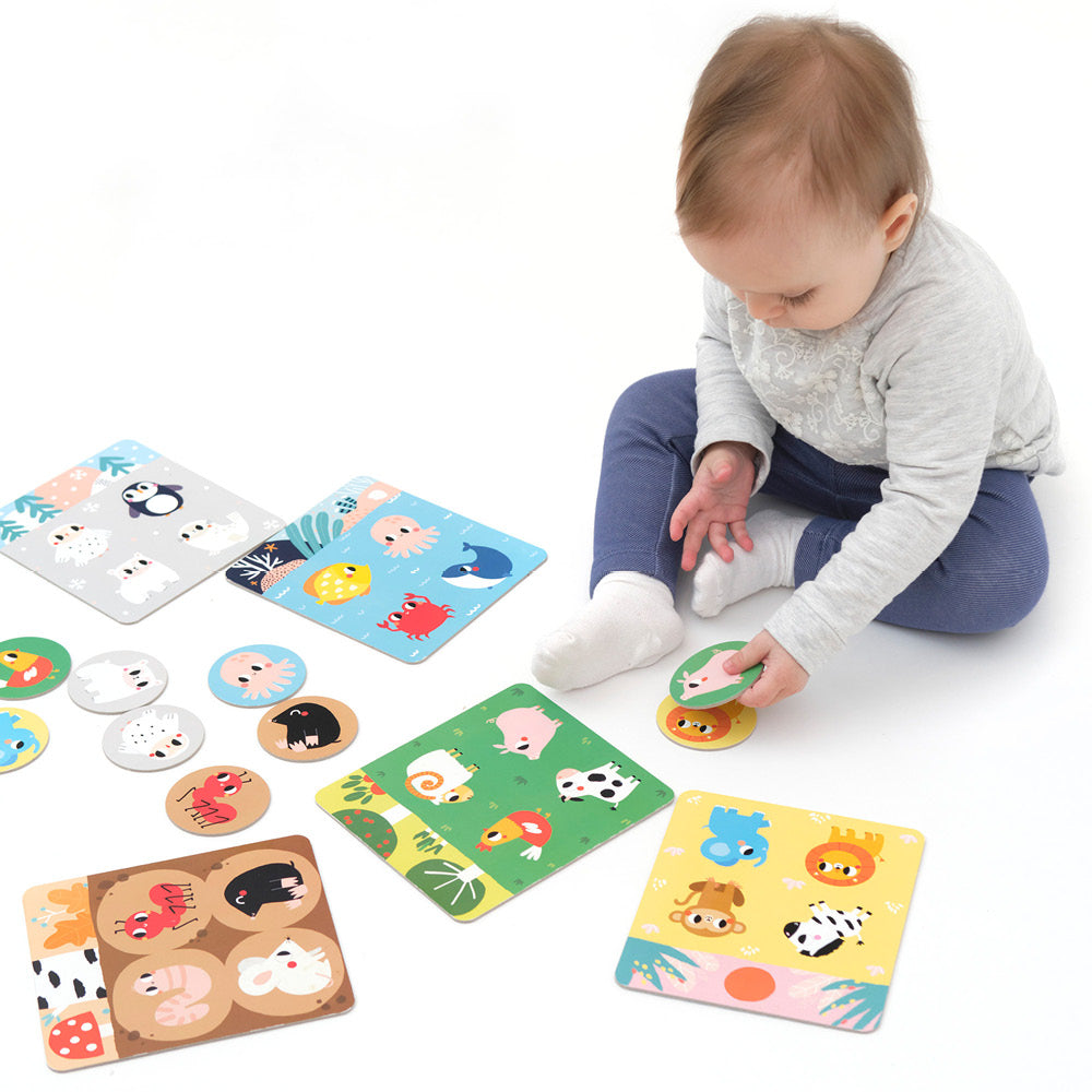 Toddler playing with colorful animal boards and tokens in the educational Habitat Bingo game set.