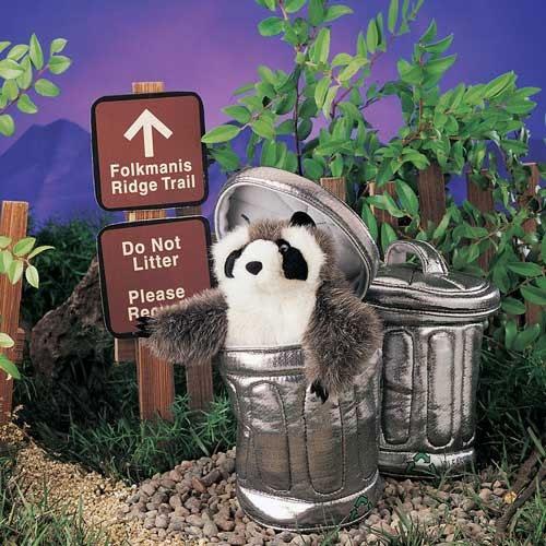 Raccoon in Garbage Can Puppet peeking out from trash can amidst greenery and trail signs in playful outdoor setting.