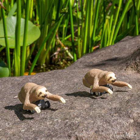 Two Racing Sloth toys made of soft vinyl on wheels set outdoors on a rock under sunlight.