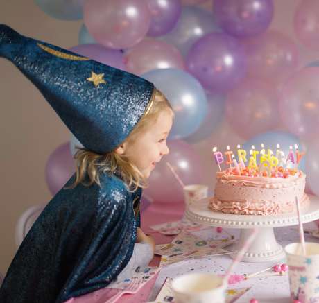 Child wearing Starry Night Wizard Cape & Hat at a birthday party with pink cake and balloons in the background