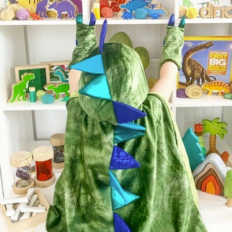 Child wearing a green textured velour Dragon Cape with Claws featuring blue spikes and stuffed claws in a playroom setting.
